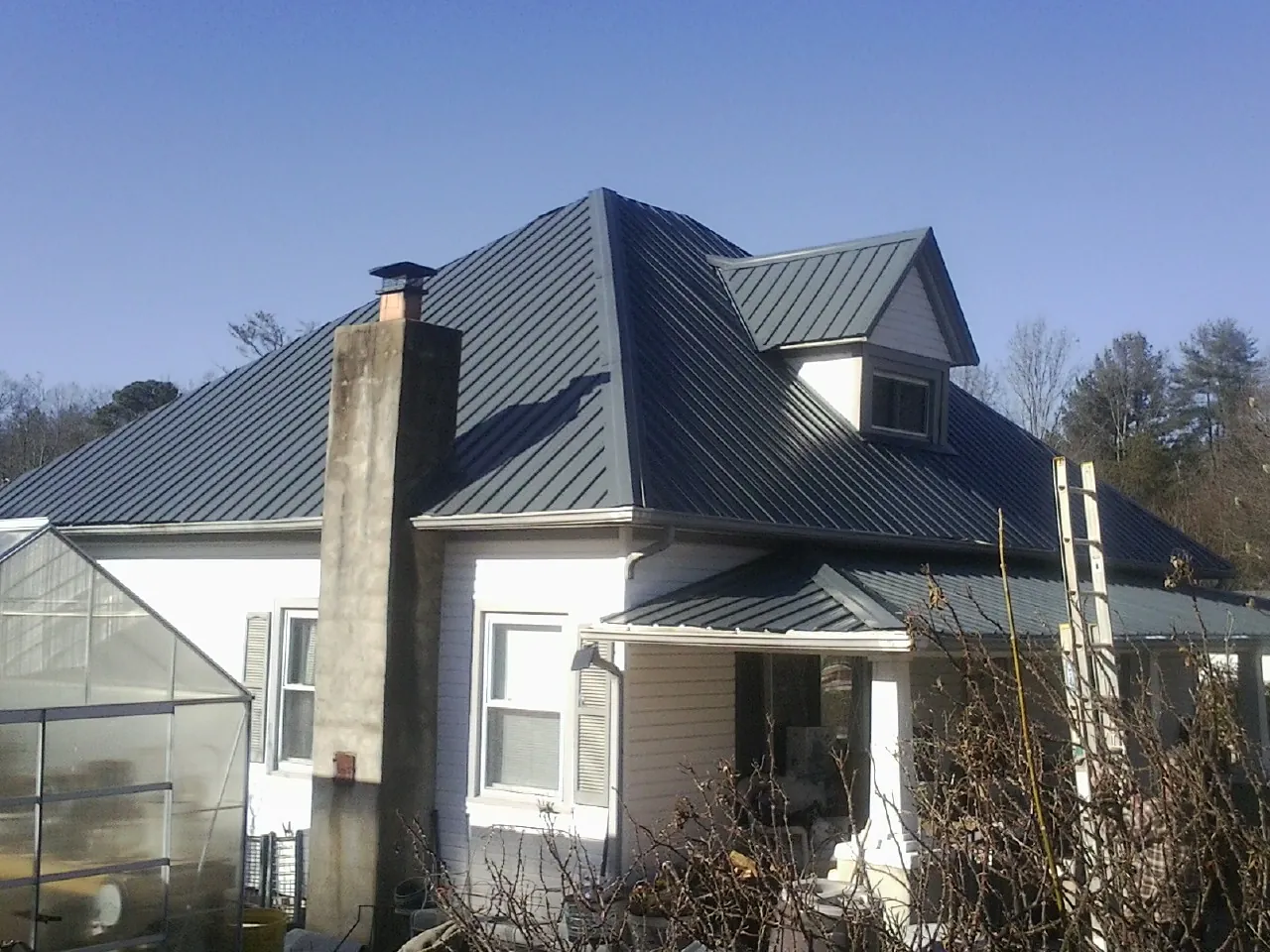 Dark blue standing seam metal roof on a white farmhouse with dormer — Slate & Tile Roof Repair by Roofing Brothers in Moran