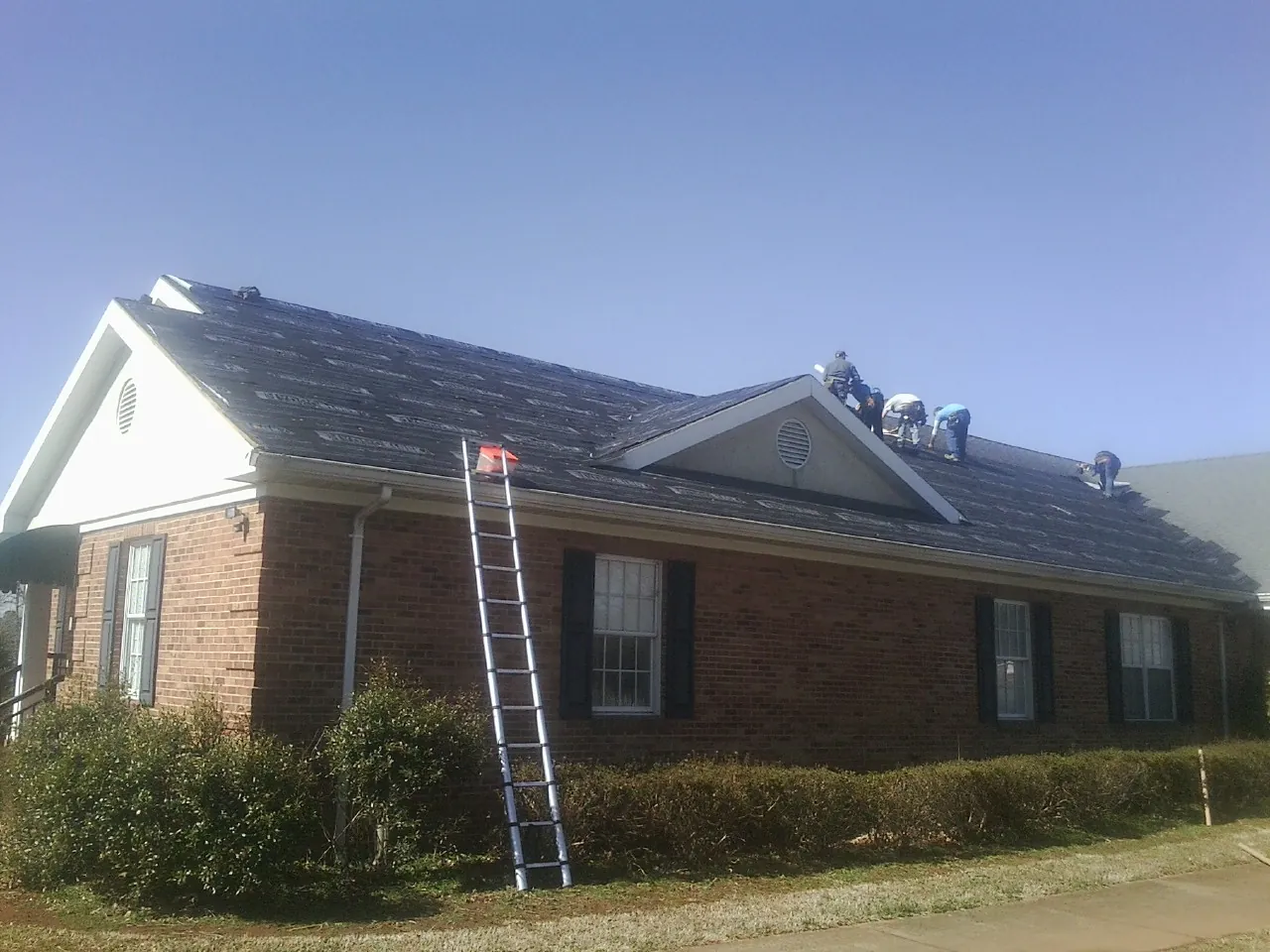 Crew tearing shingles off a brick ranch roof with a ladder set — Emergency Roof Repair work by our crew in Moran