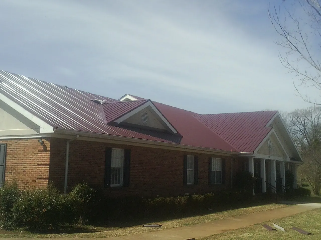 Red metal roof with gabled entries on a long brick building, from a Hail Damage Roof Repair job in Moran