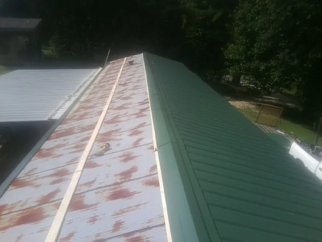 Old rusted panels beside newly installed green metal roofing — Wind Damage Roof Repair by Roofing Brothers in Moran