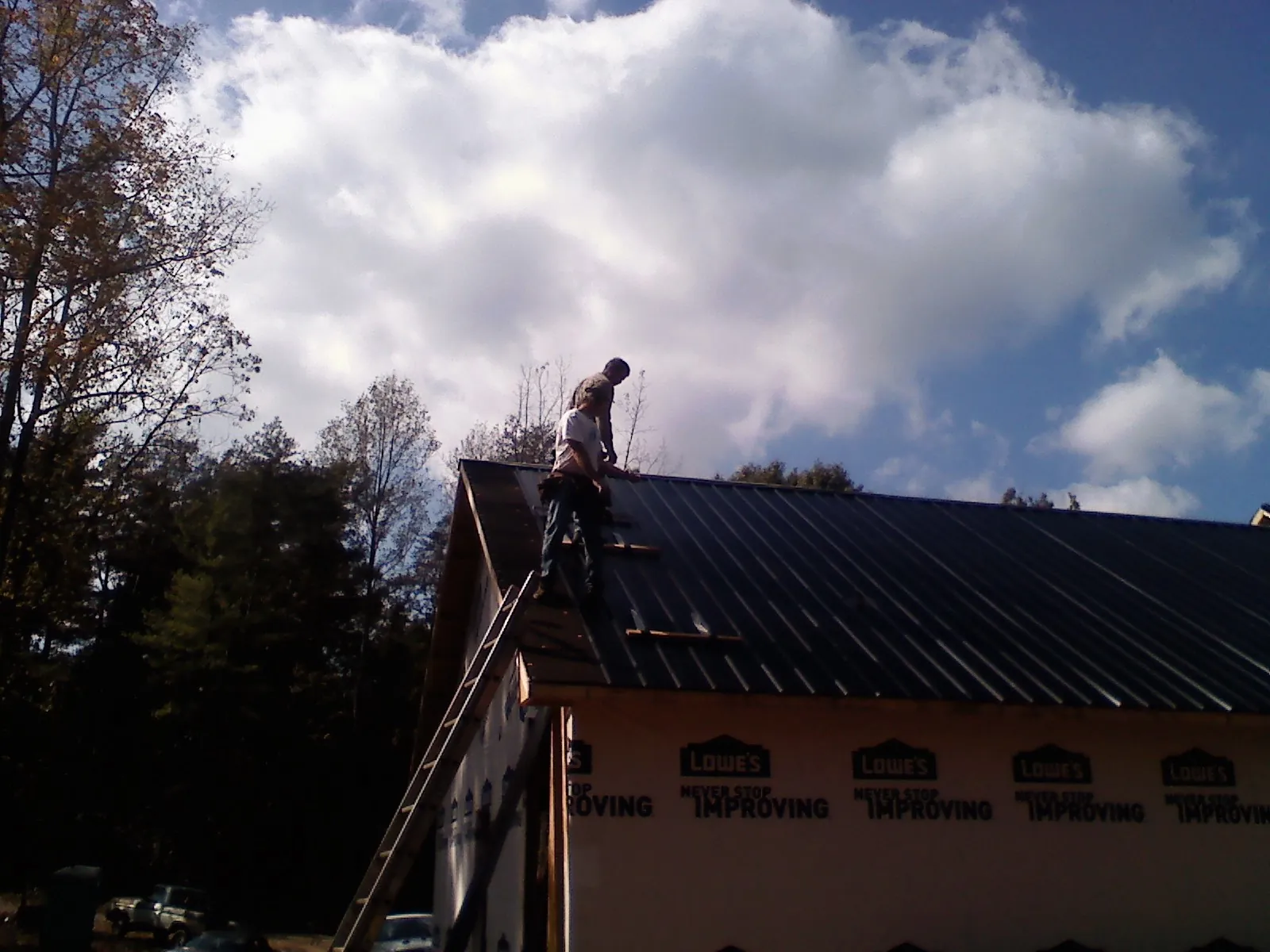 Roofer fastening dark metal panels high against a cloudy sky, from a Roof Inspection job in Moran