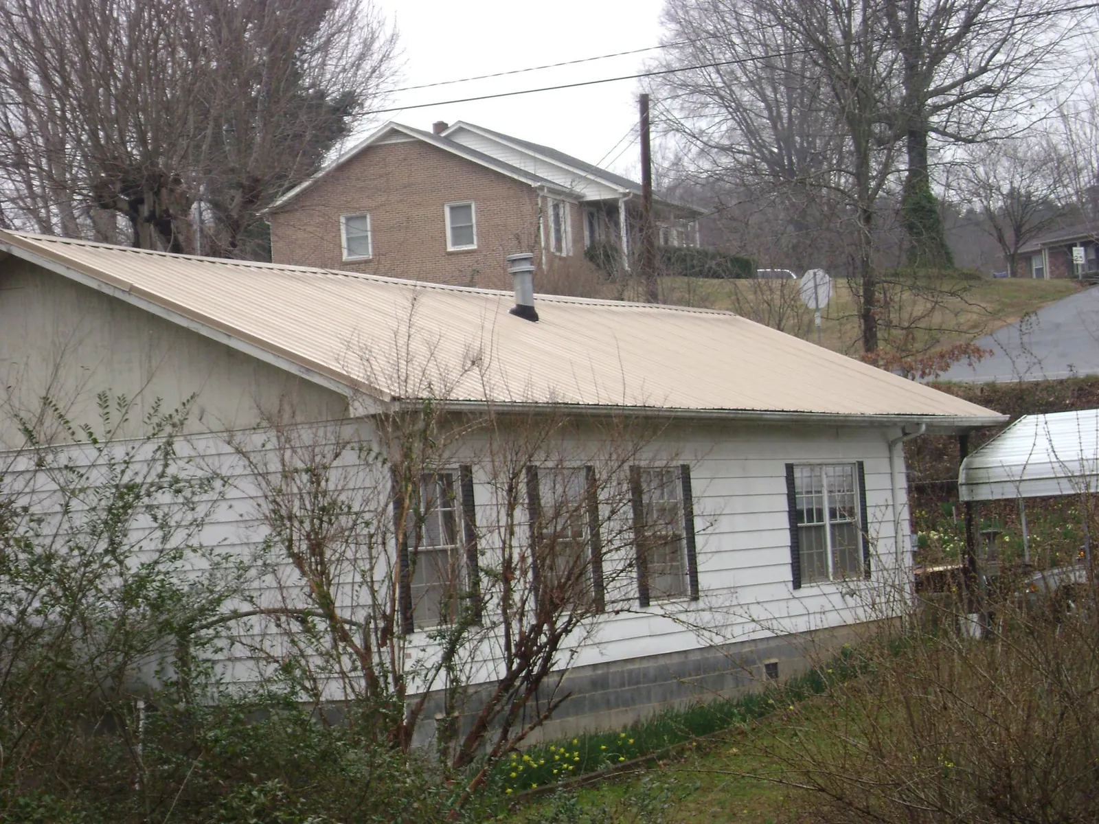 Tan metal roof on a white sided house set into a hillside — Commercial Roofing by Roofing Brothers in Moran