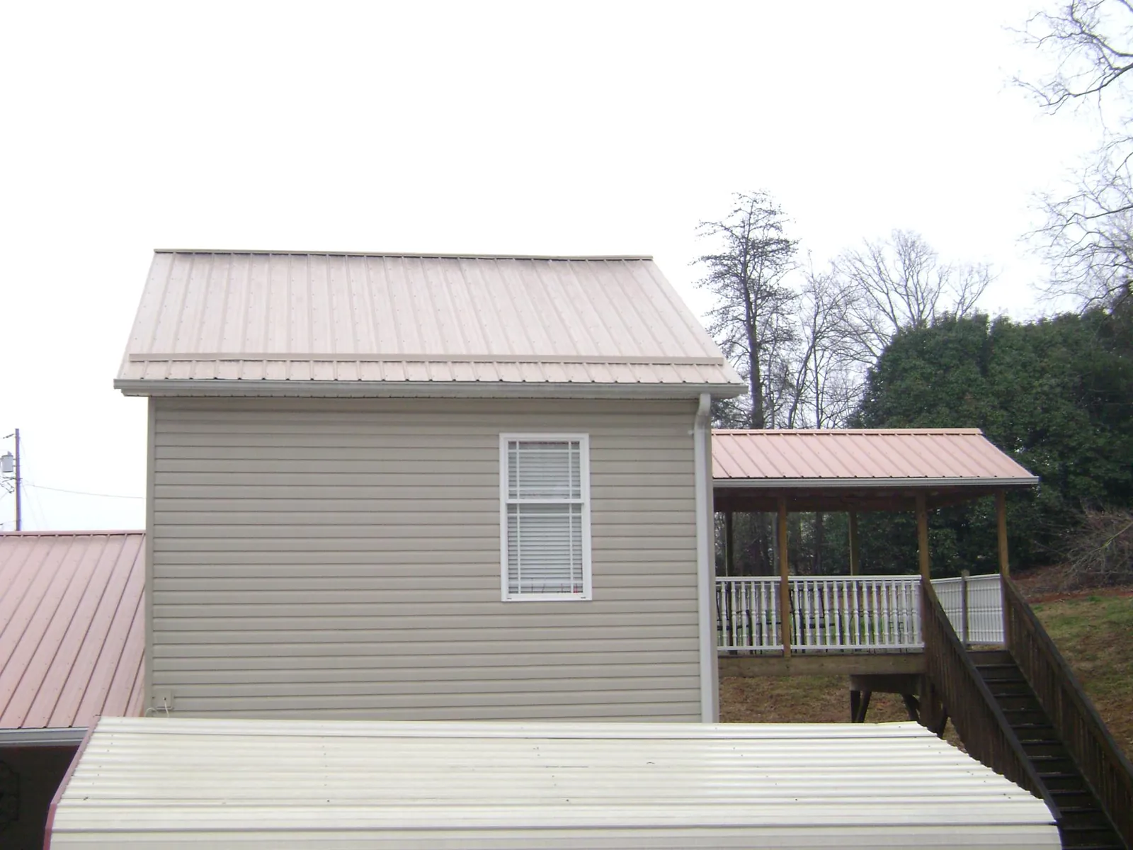 Tan metal roofs on a two story addition and attached porch, from a Roof Replacement job in Moran